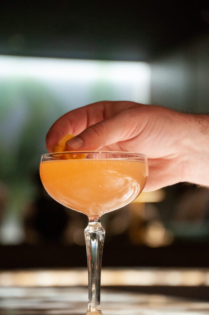 Hand garnishing a orange cocktail. Tycoon Flower Mound- upscale restaurant and bar